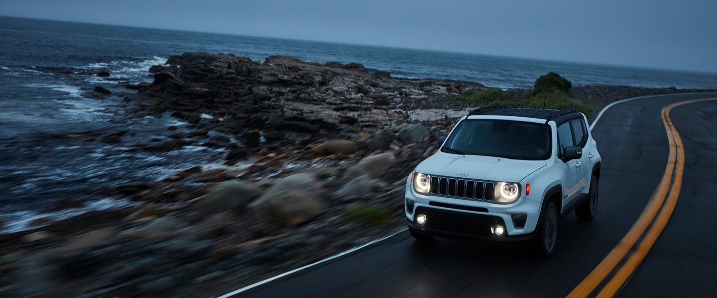 A 2020 Jeep Renegade being driven along a rocky seaside highway at dusk.