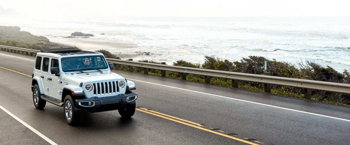 A white 2020 Jeep Wrangler Sahara on a road beside the water.