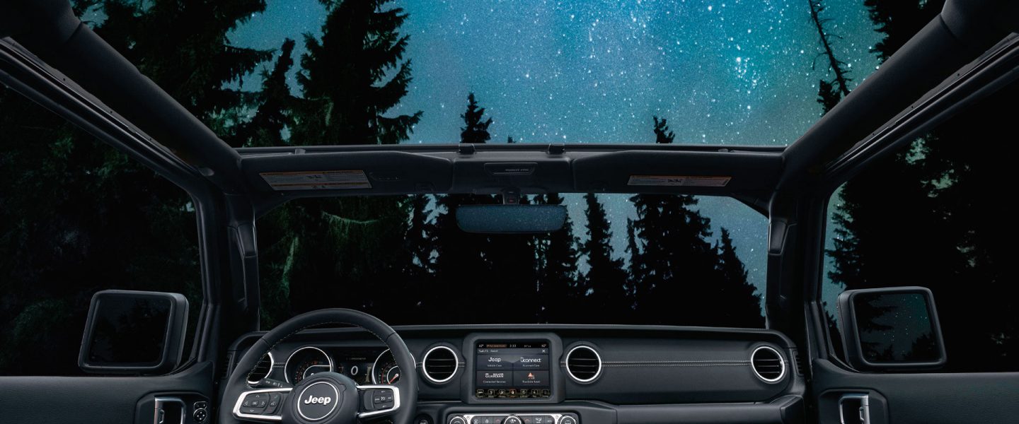 An interior view of the 2020 Jeep Wrangler with its top off and a sky full of stars visible outside.
