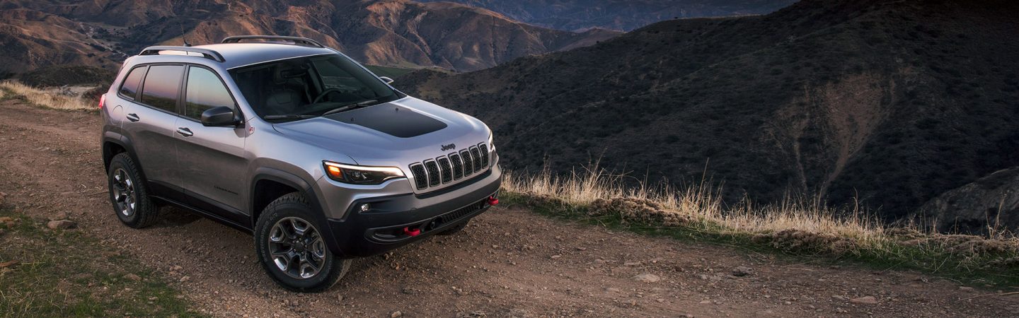 A 2021 Jeep Cherokee Trailhawk parked on the edge of a cliff in the mountains at sunset.