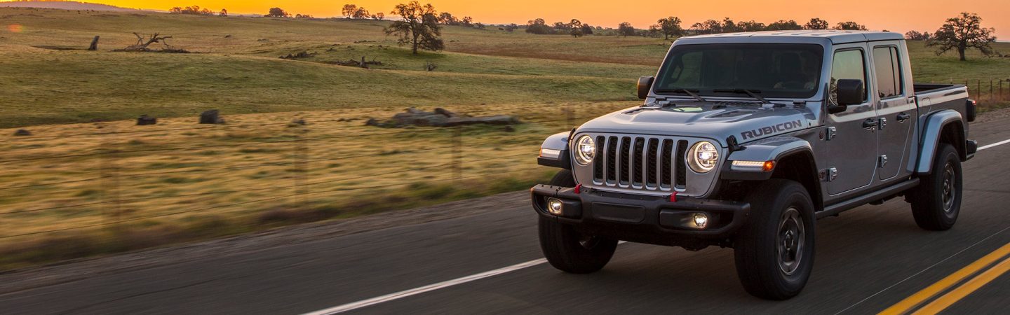 A 2021 Jeep Gladiator Rubicon being driven on a highway near grassy fields at sunset.