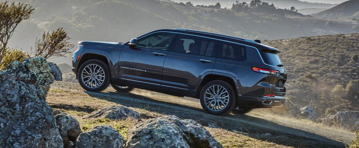 The 2021 Jeep Grand Cherokee L Summit Reserve parked facing uphill on a grassy track in the mountains.