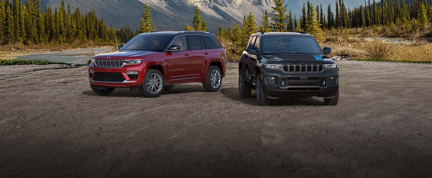 A 2022 Jeep Grand Cherokee Summit and Grand Cherokee Trailhawk 4xe parked on a sandy plain with mountains in the background.