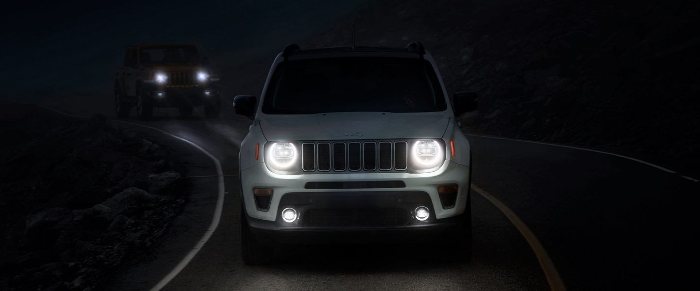 A head-on view of a 2021 Jeep Renegade on a dark road at night with its headlamps lit.