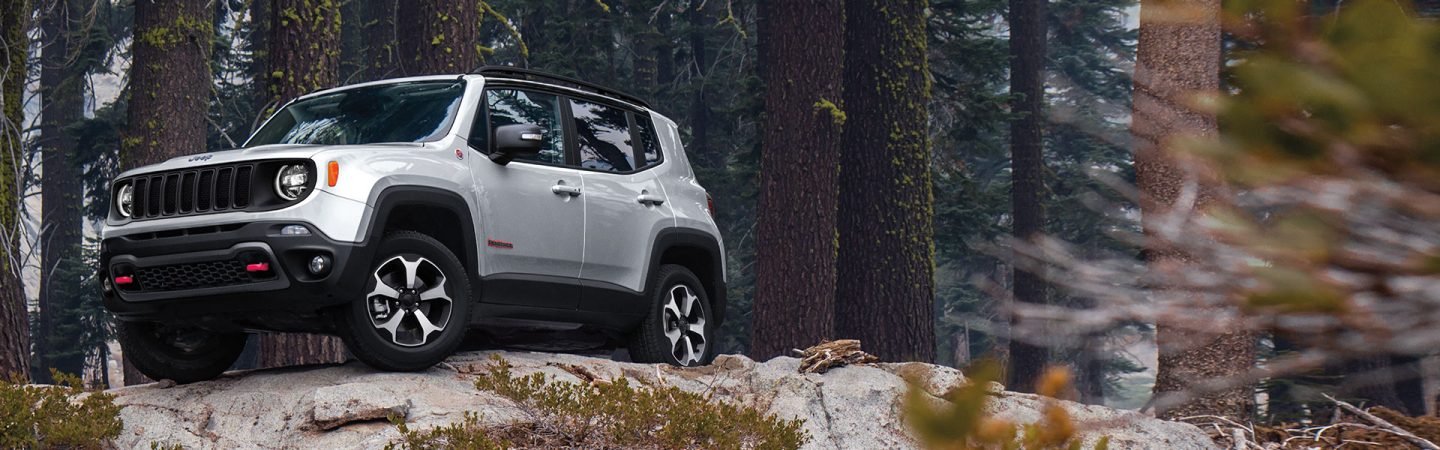 A white 2021 Jeep Renegade Trailhawk parked on a rocky hilltop in the woods.