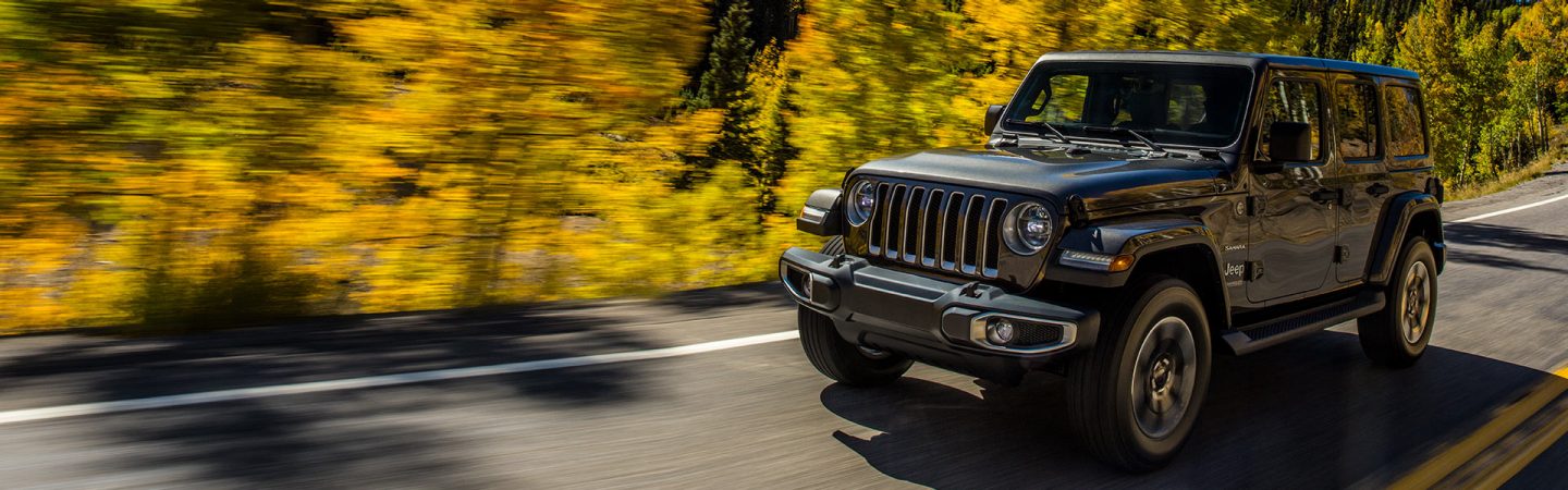 The 2021 Jeep Wrangler Sahara being driven on a highway in the woods.