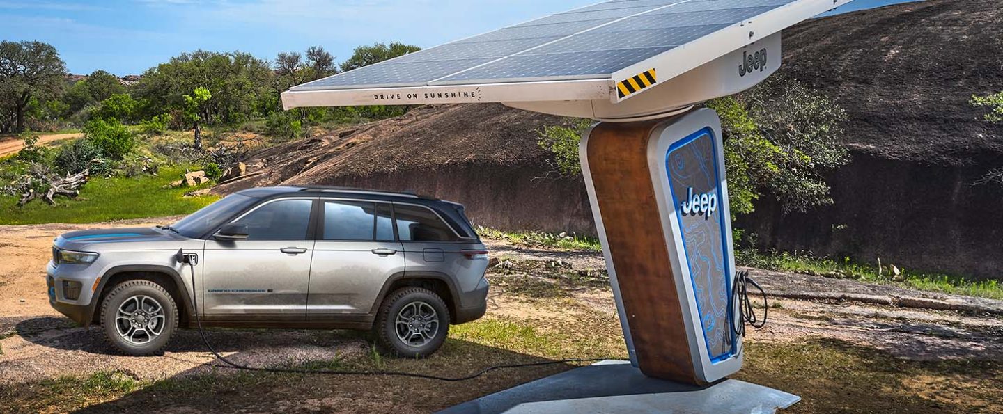 The 2022 Jeep Grand Cherokee Trailhawk 4xe connected to a charging station at the foot of a mountain, no road in sight.