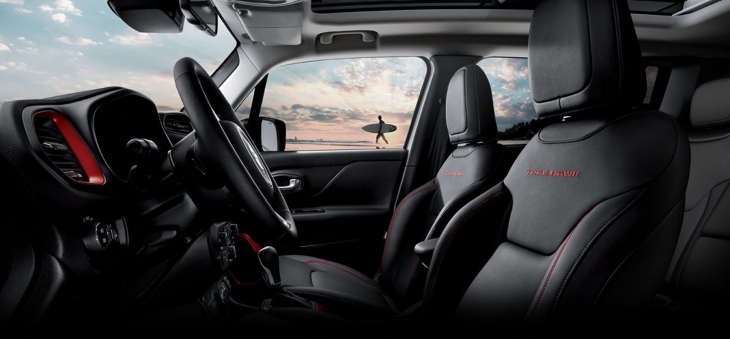 The luxurious interior of the 2022 Jeep Renegade Trailhawk with a beach vista and a surfer visible through the window.