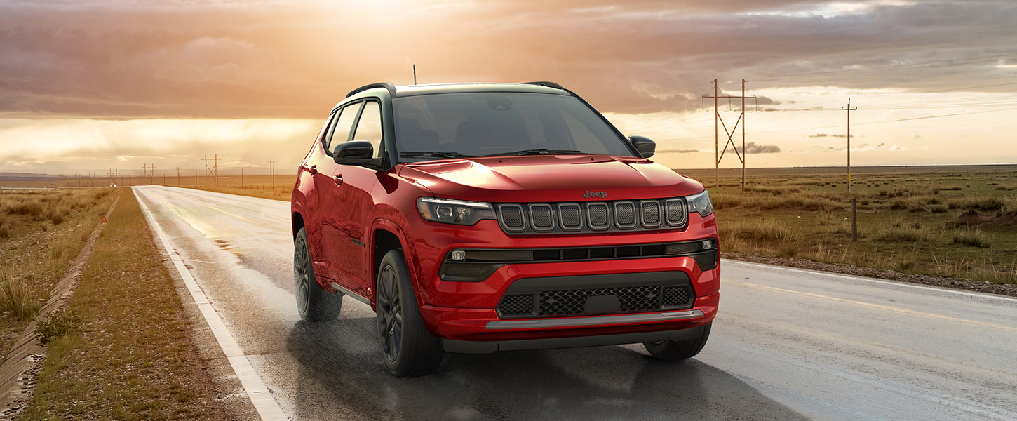 A slider that when pulled to the right reveals a 2023 Jeep Compass Limited being driven on a highway between two open fields at sunset; and when pulled to the left reveals the same 2023 Jeep Compass Limited being driven through a dark, heavy rainstorm on a highway between two open fields.