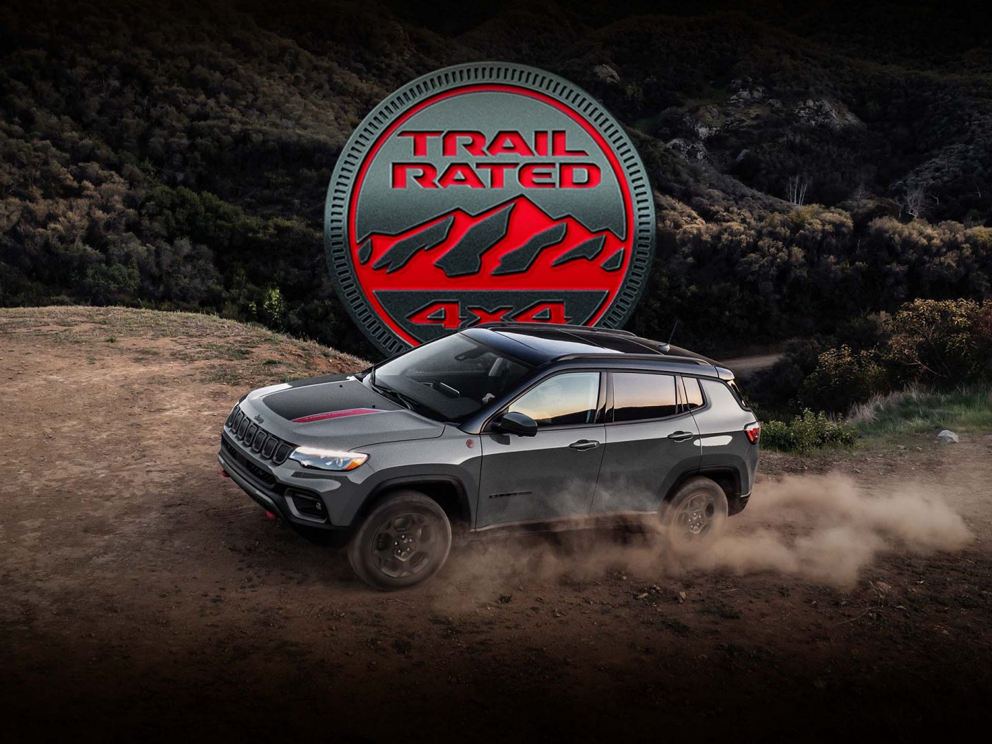 A 2023 Jeep Compass Trailhawk being driven on a hill off-road, with the tires kicking up dust. The Trail Rated 4x4 badge.