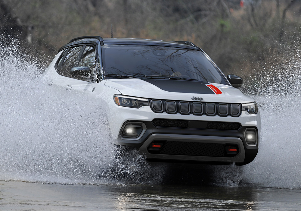 A 2023 Jeep Compass Trailhawk being driven through a stream with water splashing up the sides of the doors.