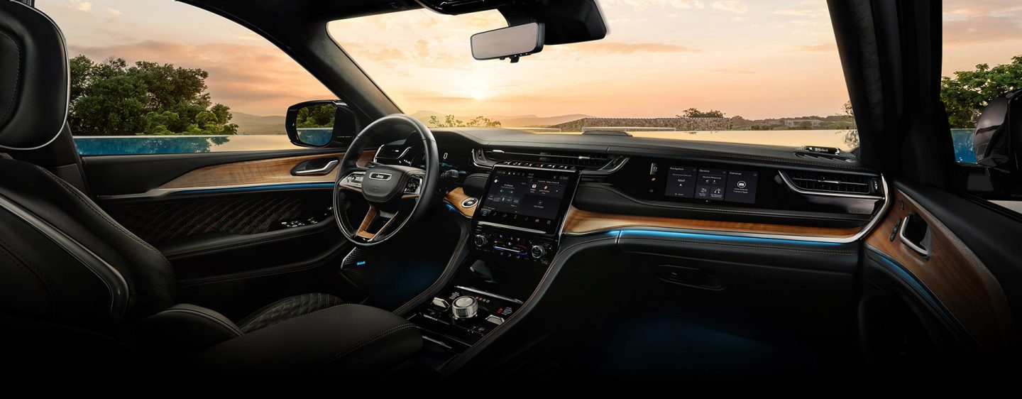 The cockpit of the 2023 Jeep Grand Cherokee Summit Reserve with a view of a lake at sunset through the windshield.