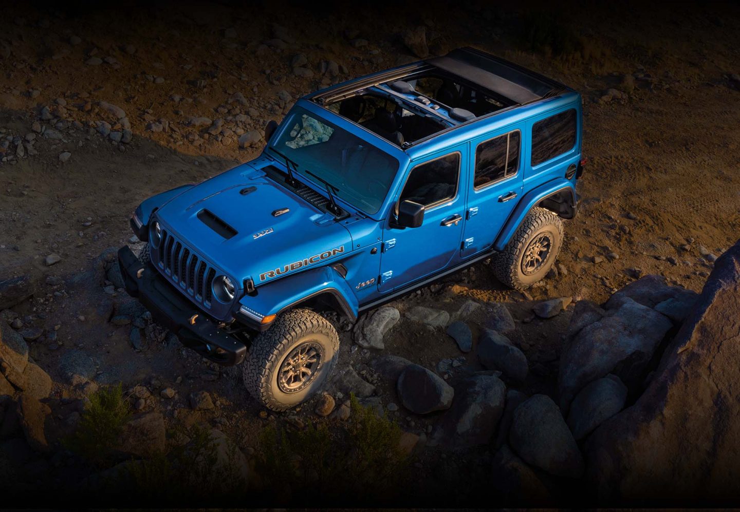 The 2023 Jeep Wrangler Rubicon 392 with its Sky One-Touch Power Top open as it is driven up a rocky slope.