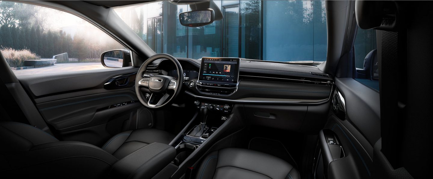 The front seat area in the 2026 Jeep Compass, focusing on the seats, steering wheel, Digital Cluster Display, Uconnect touchscreen and center stack controls.