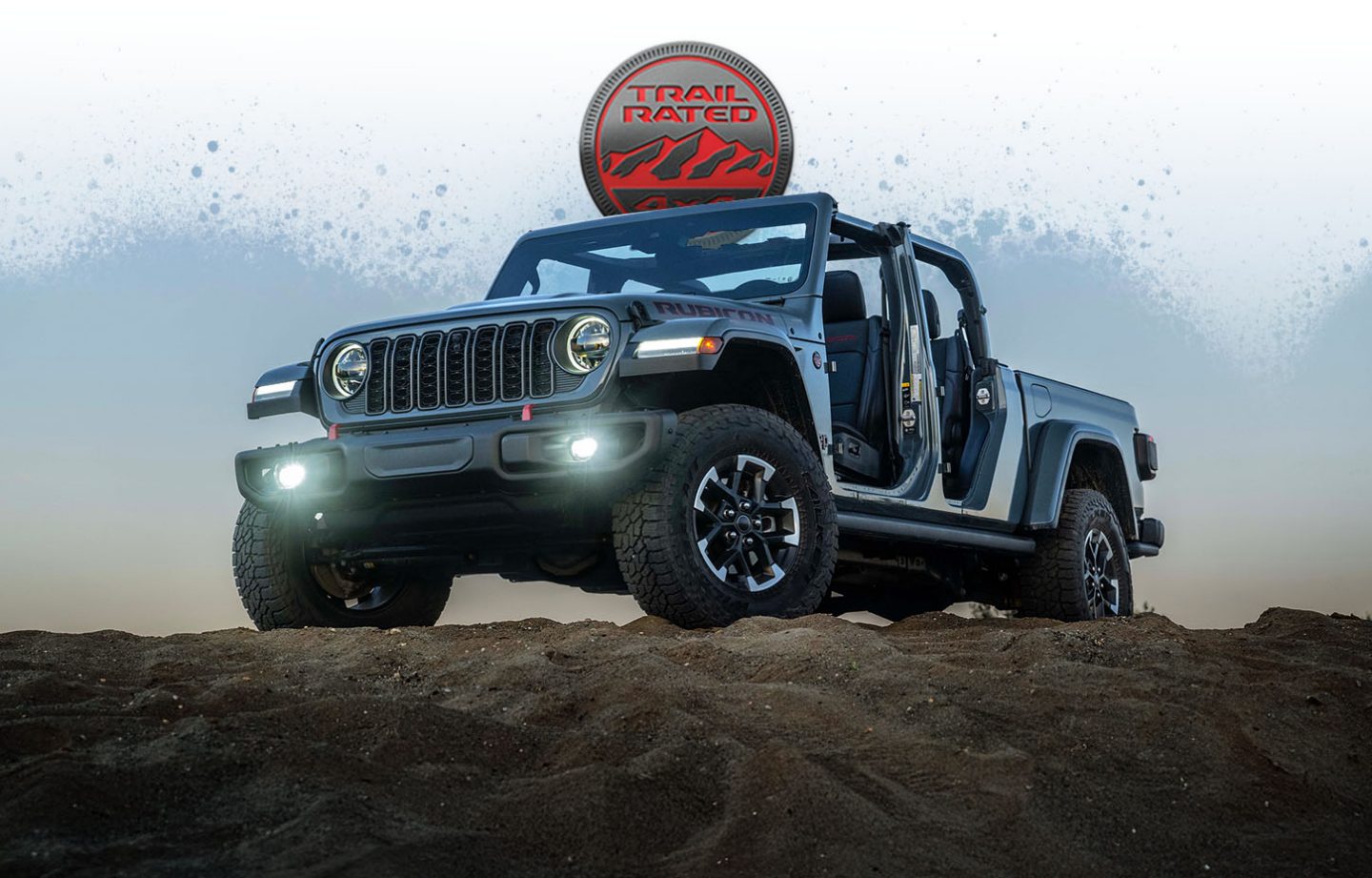 A gray 2026 Jeep Gladiator Rubicon with its doors removed, parked on the top of a rocky hill. The Trail Rated badge.