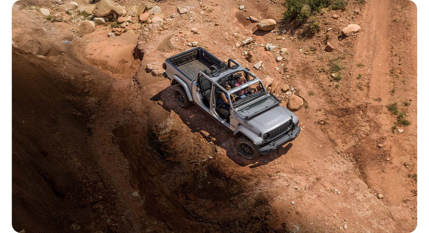 A top-down angle of a gray 2026 Jeep Willys with its doors and top removed, traveling on a rocky trail off-road.