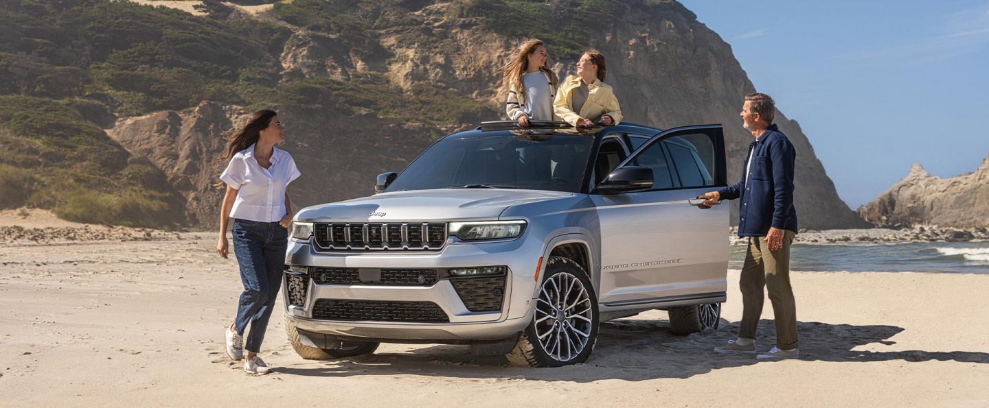 A passenger-side profile of a black 2026 Jeep Grand Cherokee L Summit parked in the winding driveway of a large home.