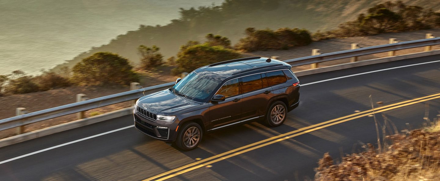 A gray 2026 Jeep Grand Cherokee Summit traveling down a coastal highway.