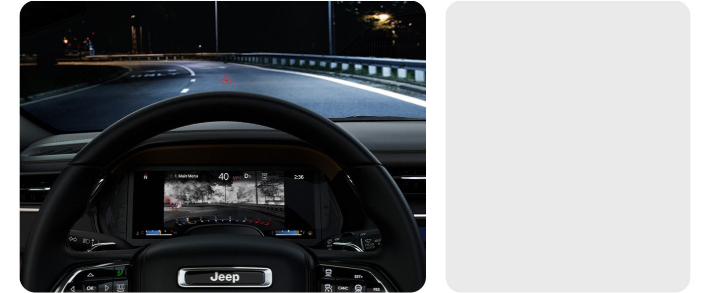 A dark highway ahead, visible through the windshield of the 2026 Jeep Grand Cherokee, as the Digital Cluster displays a thermal image of the same road with a deer standing beside it, not noticeable with the naked eye.
