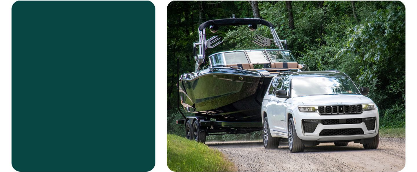 A white 2026 Jeep Grand Cherokee Summit traveling down a dirt road towing a large motorboat.