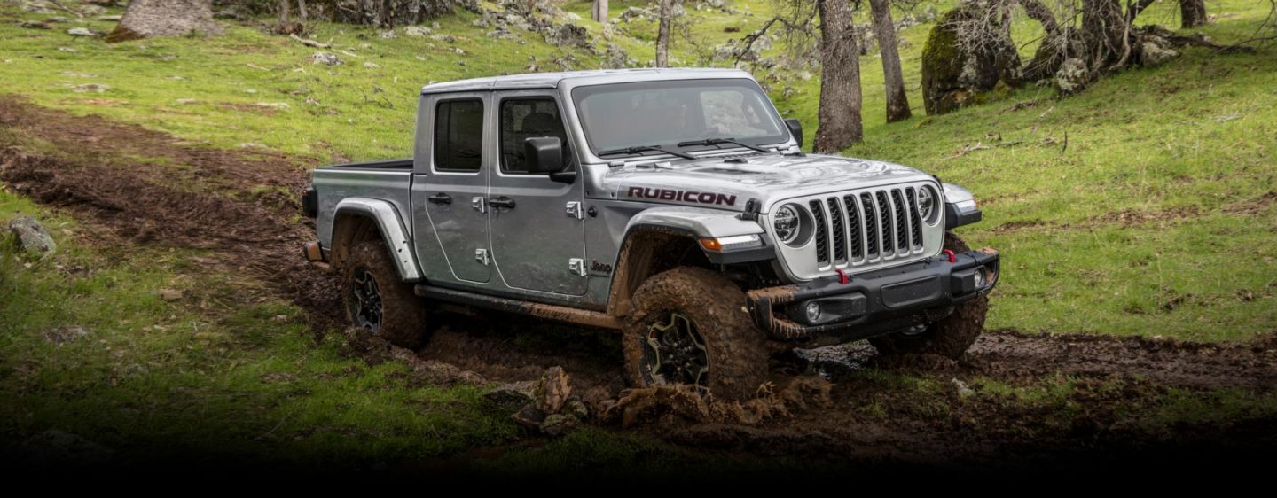 The 2023 Jeep Gladiator Rubicon being driven on a muddy trail, its wheels and lower body spattered with mud.