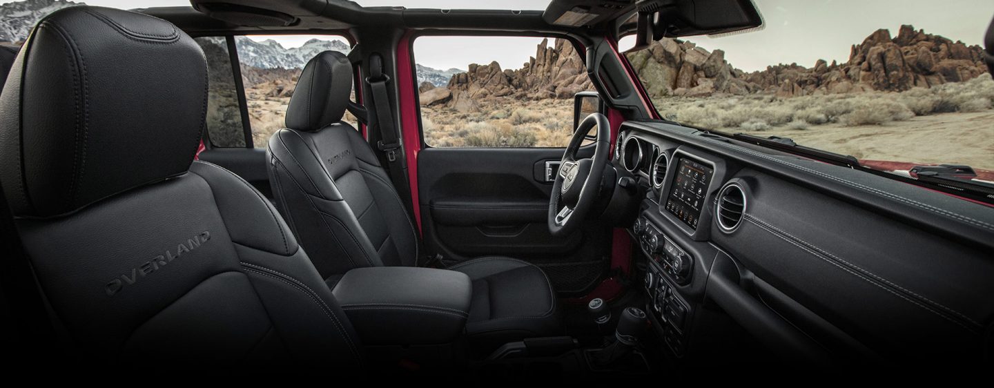 The interior of the 2023 Jeep Gladiator Overland with its top off, focusing on the front seats and dash.