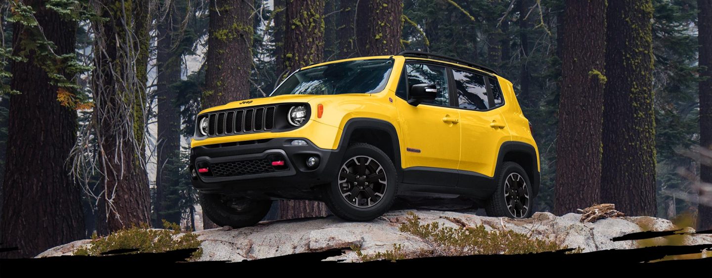 A yellow 2023 Jeep Renegade Trailhawk parked on bare rock with trees in the background.