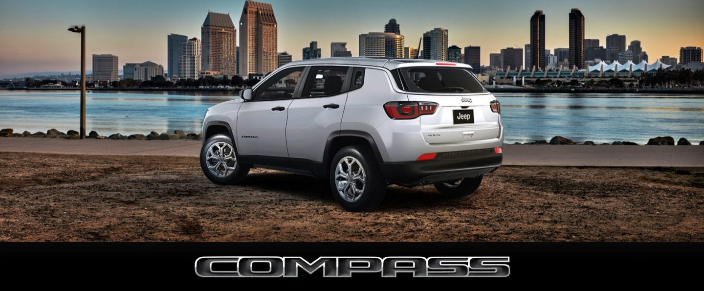 A gray 2024 Jeep Compass Trailhawk with a black and red hood insert being driven down a snow-covered hill in the mountains. Compass.