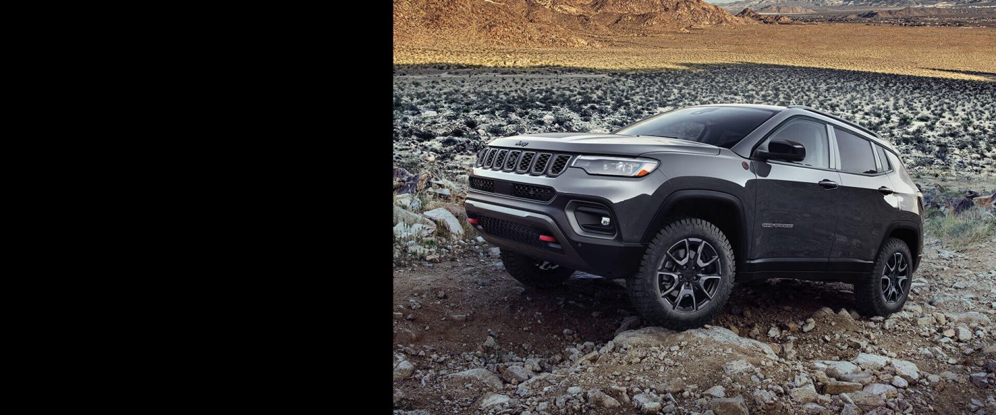 A gray 2024 Jeep Compass Trailhawk crawling over large and small rocks and stones off-road.