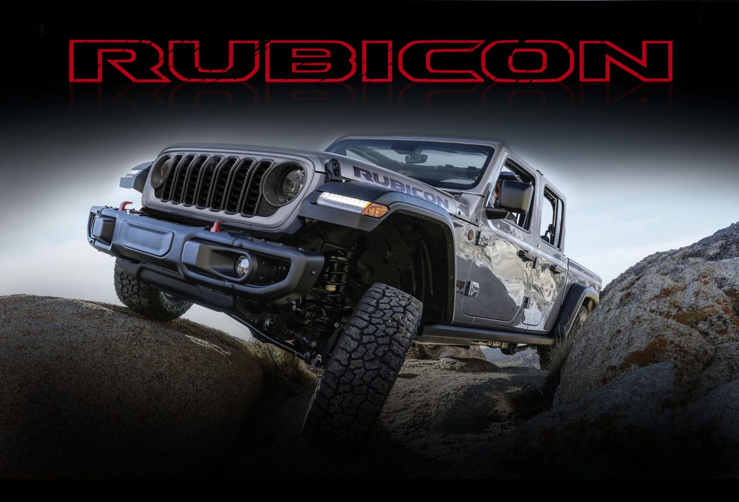 A silver 2024 Jeep Gladiator Rubicon with its roof removed, crawling over rocky terrain with one wheel elevated as it climbs a boulder.
