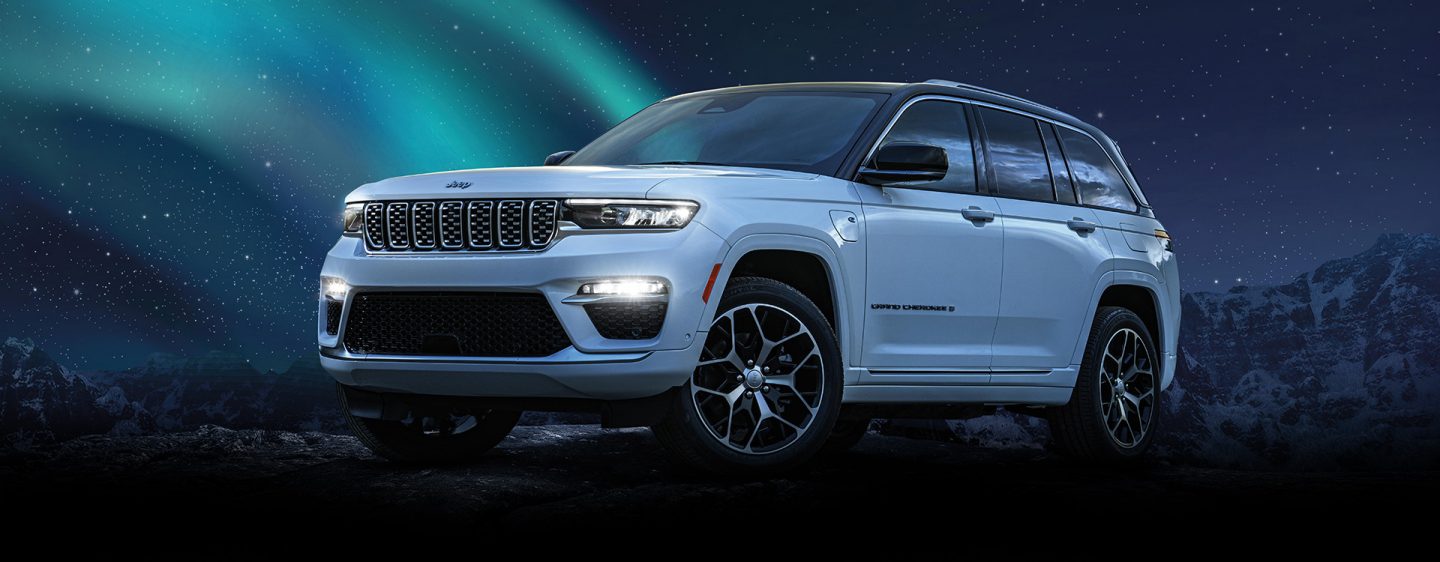 The 2024 Jeep Grand Cherokee Summit Reserve 4xe parked on a clearing off-road at night, with the northern lights in the background.
