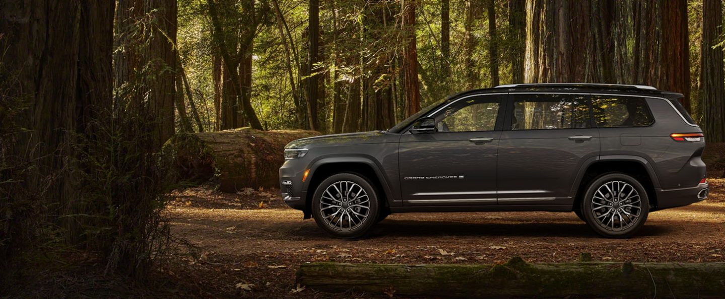 The driver-side profile of a 2024 Jeep Grand Cherokee L Summit Reserve, parked in the woods.