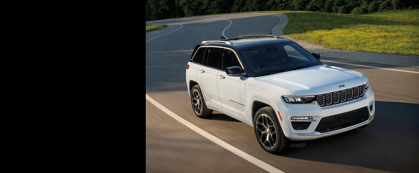 A white 2024 Jeep Grand Cherokee Summit Reserve being driven on a curved highway.