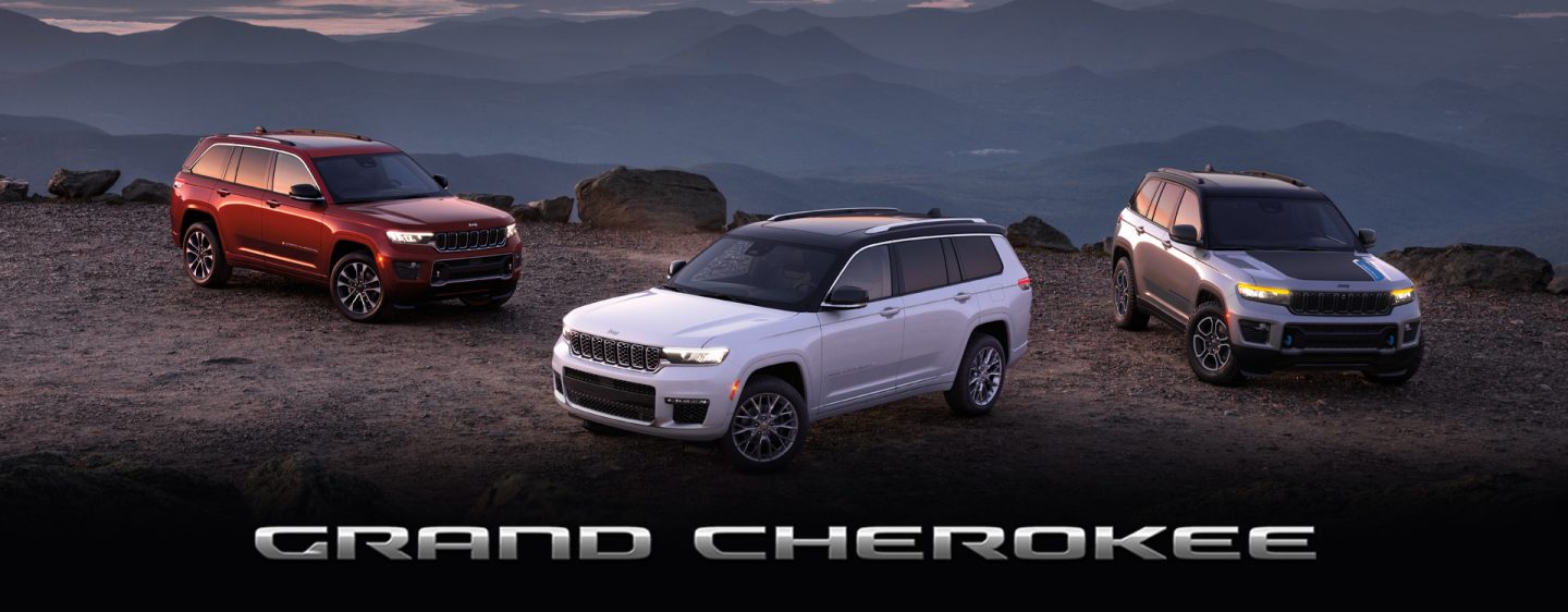 Three 2024 Jeep Grand Cherokee models parked on a rocky clearing at dusk, with mountains in the background; from left to right: a red Grand Cherokee Overland, white Grand Cherokee Summit and silver Grand Cherokee Trailhawk 4xe.